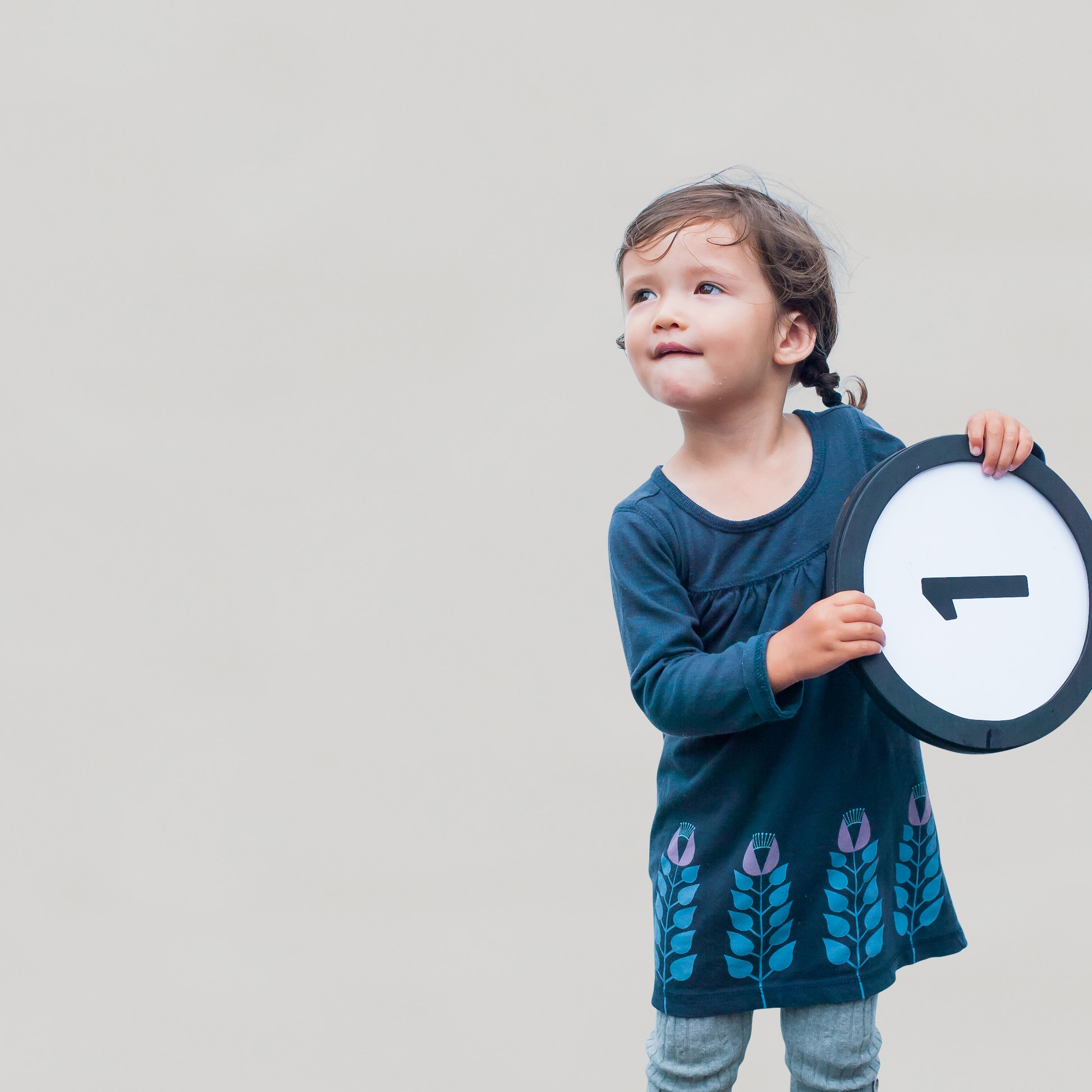 1 year old girl in blue dress glances skyward while holding a token with the number one on it. This digital image is part of the 1 to Infinity portrait photography series by Danny Goldfield.